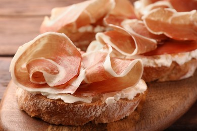 Photo of Board of tasty sandwiches with cured ham and cream cheese on table, closeup