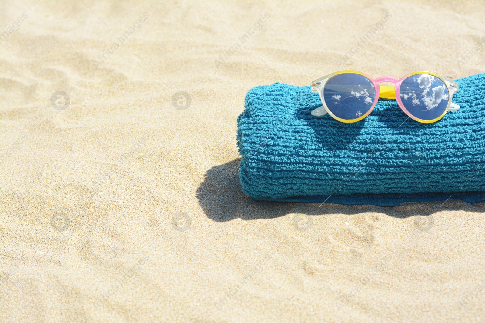 Photo of Towel with stylish sunglasses on sand outdoors, space for text. Beach accessories