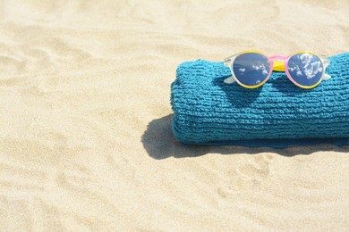 Photo of Towel with stylish sunglasses on sand outdoors, space for text. Beach accessories
