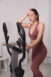 Photo of Young woman feeling tired of training on 	
elliptical machine at home