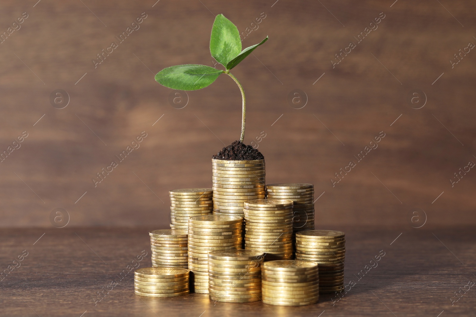 Photo of Stacks of coins with green sprout on wooden table. Investment concept
