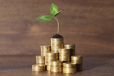 Photo of Stacks of coins with green sprout on wooden table. Investment concept