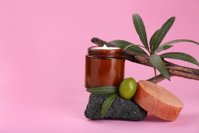 Photo of Jar of cream with olive essential oil on stone against pink background, space for text