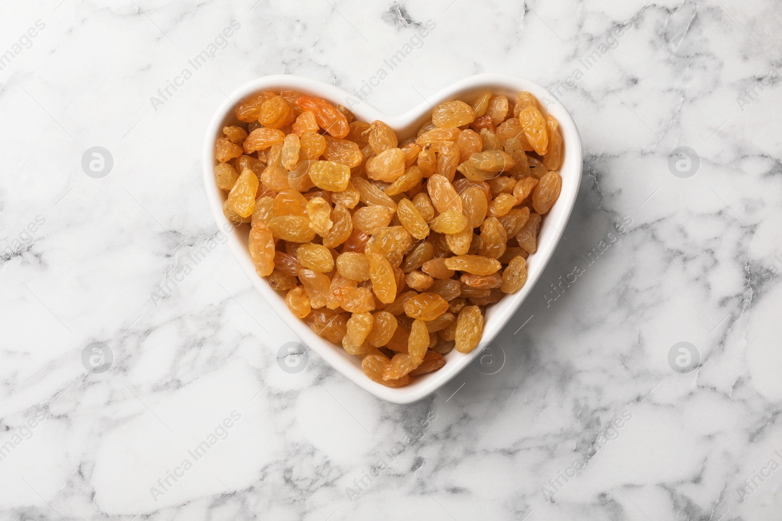 Photo of Heart shaped plate with raisins on marble background, top view. Dried fruit as healthy snack