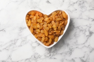 Heart shaped plate with raisins on marble background, top view. Dried fruit as healthy snack