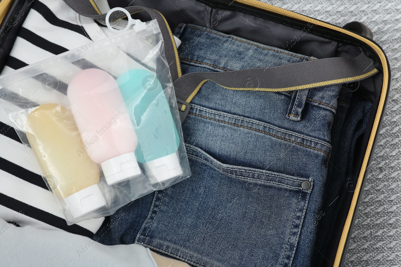 Photo of Plastic bag of cosmetic travel kit and clothes in suitcase, top view. Bath accessories