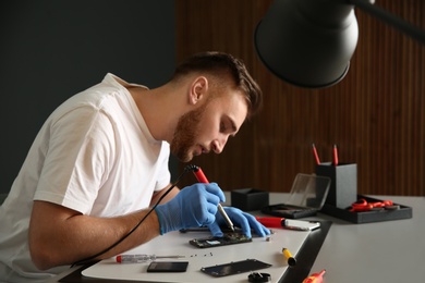 Photo of Technician repairing mobile phone at table in workshop