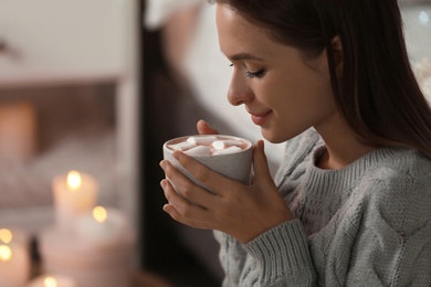 Photo of Young woman holding cup of hot cocoa with marshmallows at home. Cozy winter