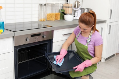 Woman cleaning oven tray with rag in kitchen