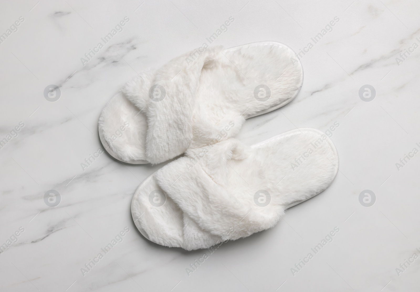 Photo of Pair of soft slippers on white marble floor, top view