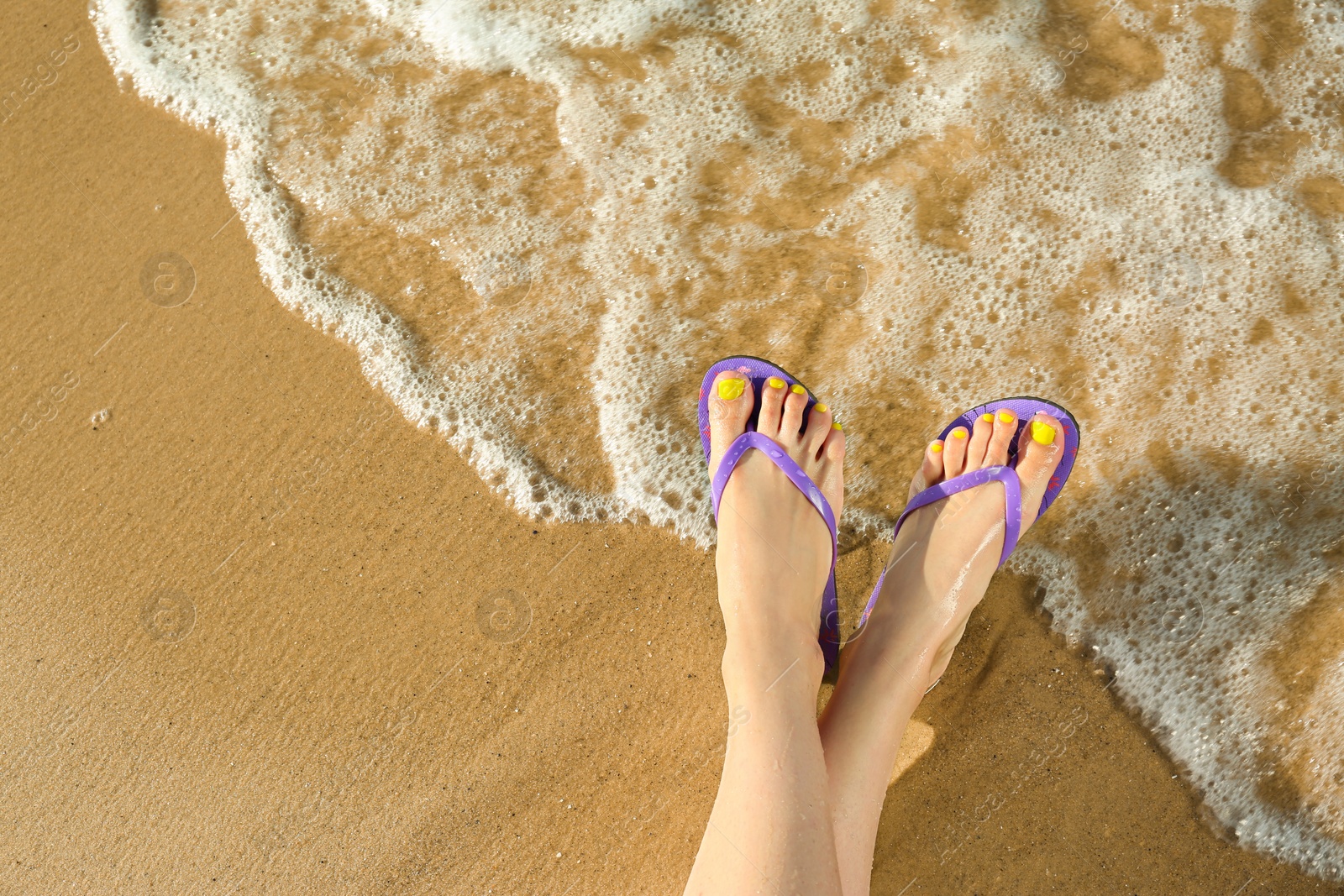 Photo of Closeup of woman with flip flops on sand near sea, space for text. Beach accessories