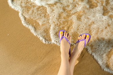 Photo of Closeup of woman with flip flops on sand near sea, space for text. Beach accessories