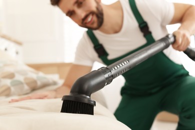 Photo of Professional janitor vacuuming sofa in living room, focus on nozzle