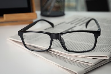 Photo of Stack of newspapers and glasses on white table indoors, closeup