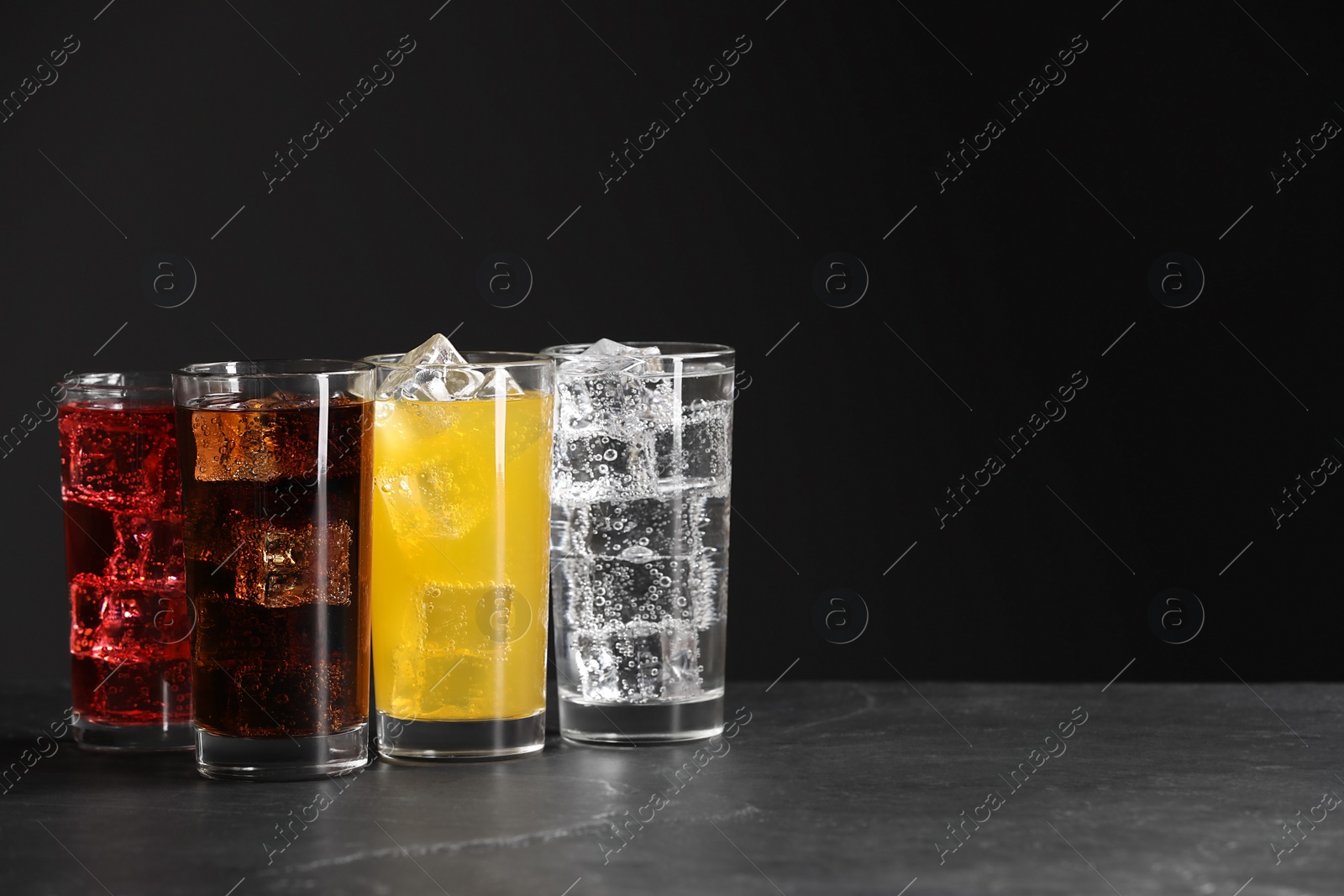 Photo of Glasses of different refreshing soda water with ice cubes on grey table, space for text