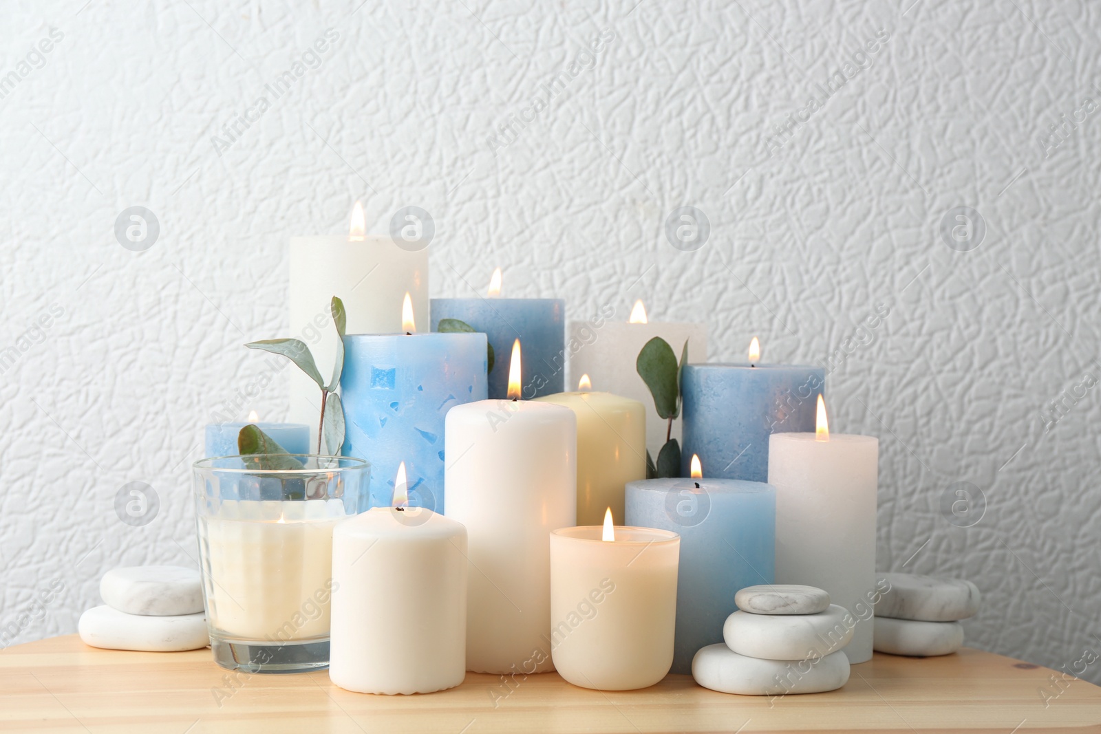Photo of Composition with burning candles on table near white wall