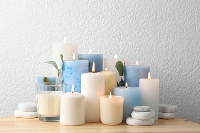 Composition with burning candles on table near white wall