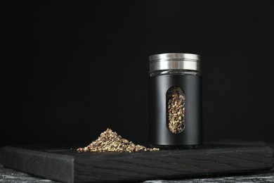 Stylish shaker with pepper on table against black background. Space for text