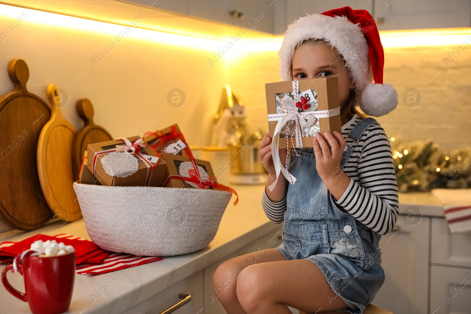 Photo of Cute little girl in Santa hat with gift from Christmas advent calendar at home