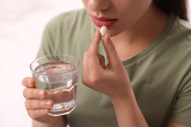 Woman with glass of water taking antidepressant pill on white background, closeup