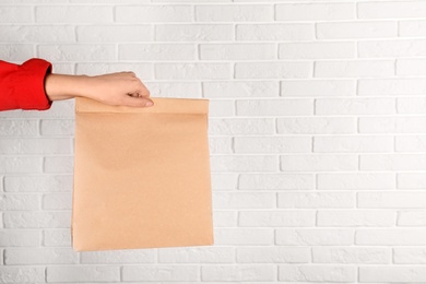 Photo of Woman holding paper bag against brick wall. Mockup for design