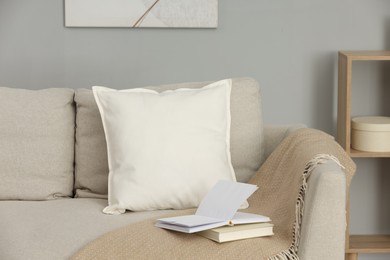 Photo of Soft white pillow, blanket and books on sofa indoors