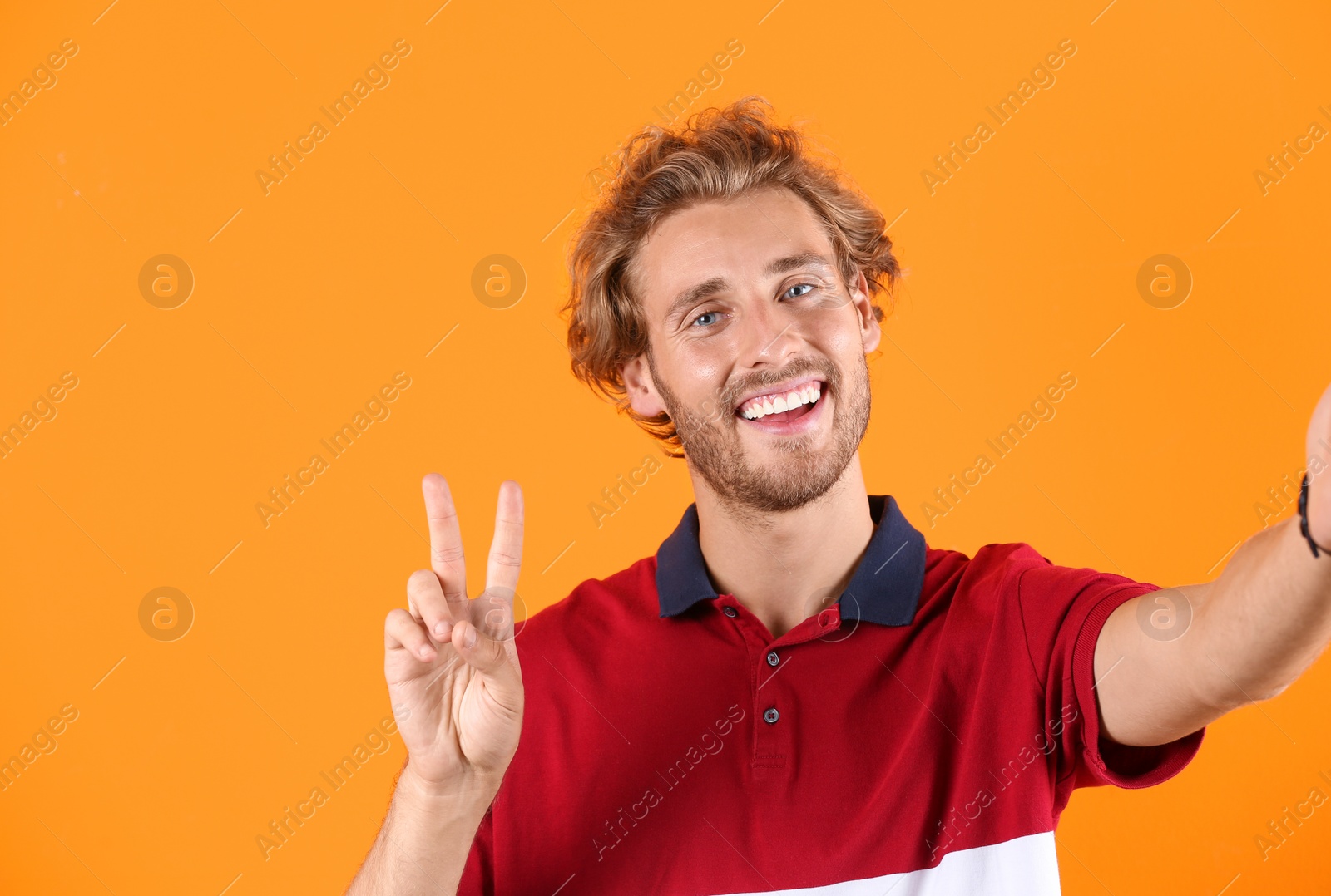 Photo of Handsome young man laughing and taking selfie on color background