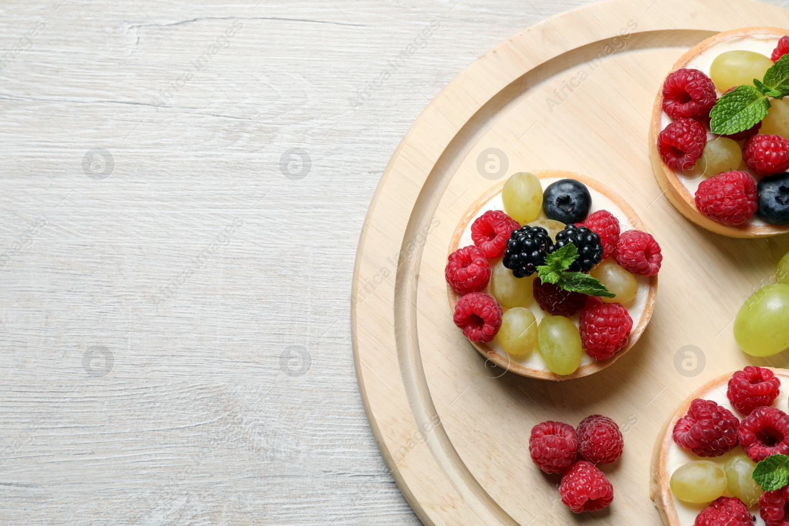 Photo of Delicious tartlets with berries on light wooden table, top view. Space for text