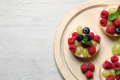 Photo of Delicious tartlets with berries on light wooden table, top view. Space for text