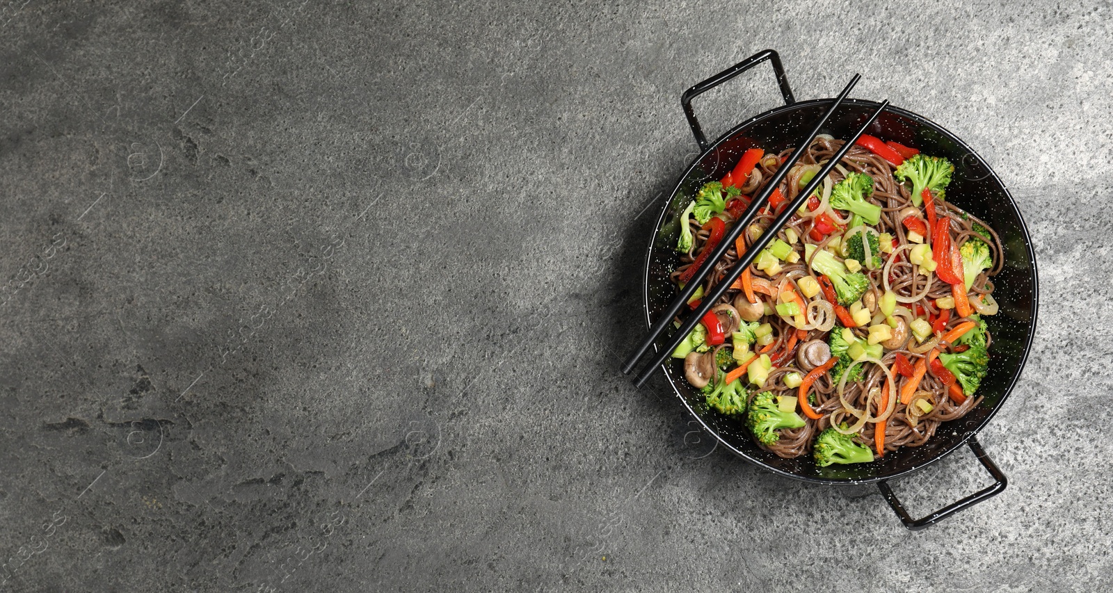 Photo of Stir fried noodles with mushrooms and vegetables in wok on grey table, top view. Space for text