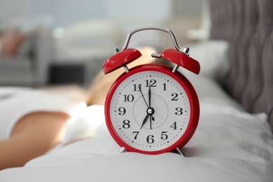 Photo of Analog alarm clock and blurred woman on background. Time of day