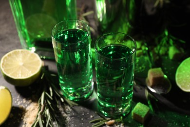 Photo of Absinthe in shot glasses, lime and rosemary on gray table, closeup. Alcoholic drink