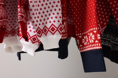 Different Christmas sweaters hanging on light background, closeup