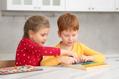 Photo of Children playing with math game kit at white marble table in kitchen. Learning mathematics with fun