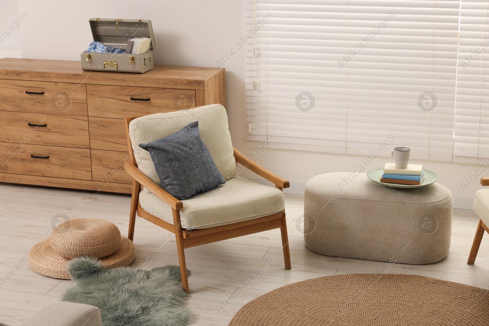 Photo of Comfortable beige armchair, ottoman and chest of drawers in living room. Interior design