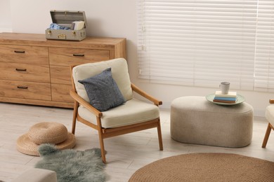 Comfortable beige armchair, ottoman and chest of drawers in living room. Interior design