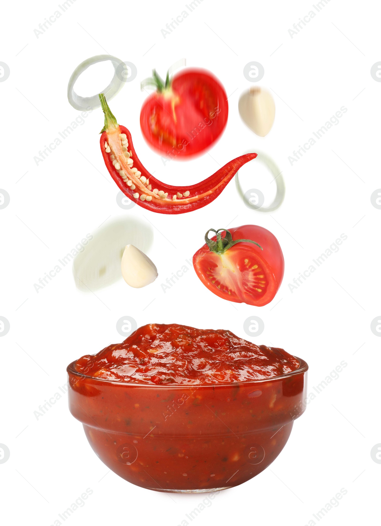 Image of Different ingredients falling into glass bowl with delicious adjika sauce on white background