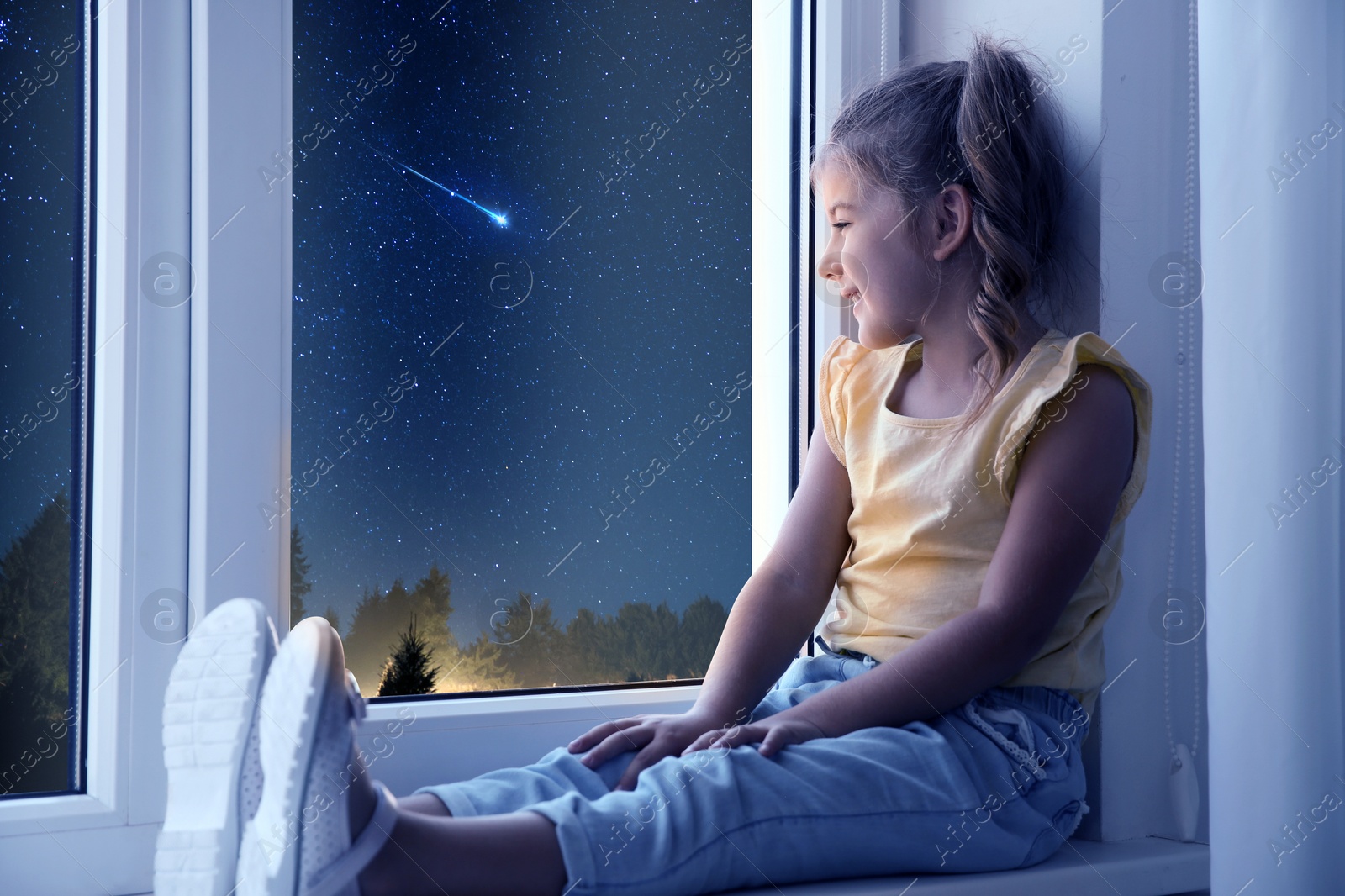 Image of Cute little girl sitting near window and looking at shooting star in beautiful night sky