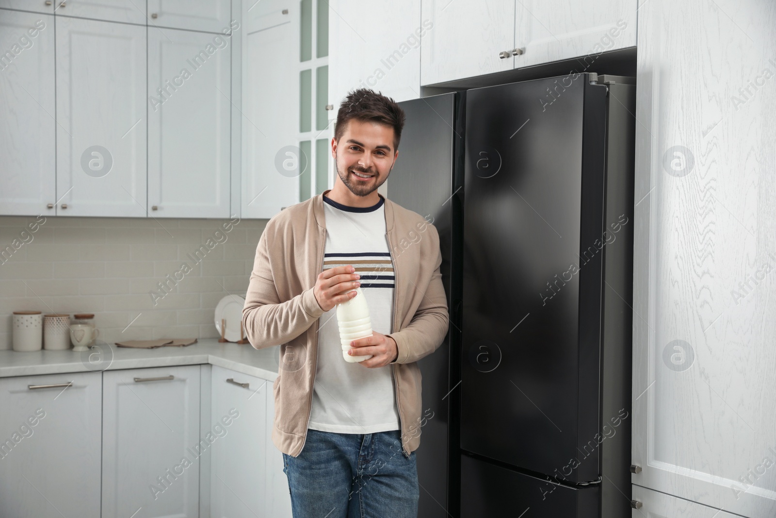 Photo of Young man with bottle of milk near refrigerator in kitchen
