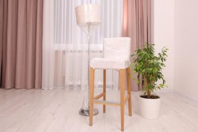 Photo of Lamp and chair wrapped in stretch film and houseplant indoors
