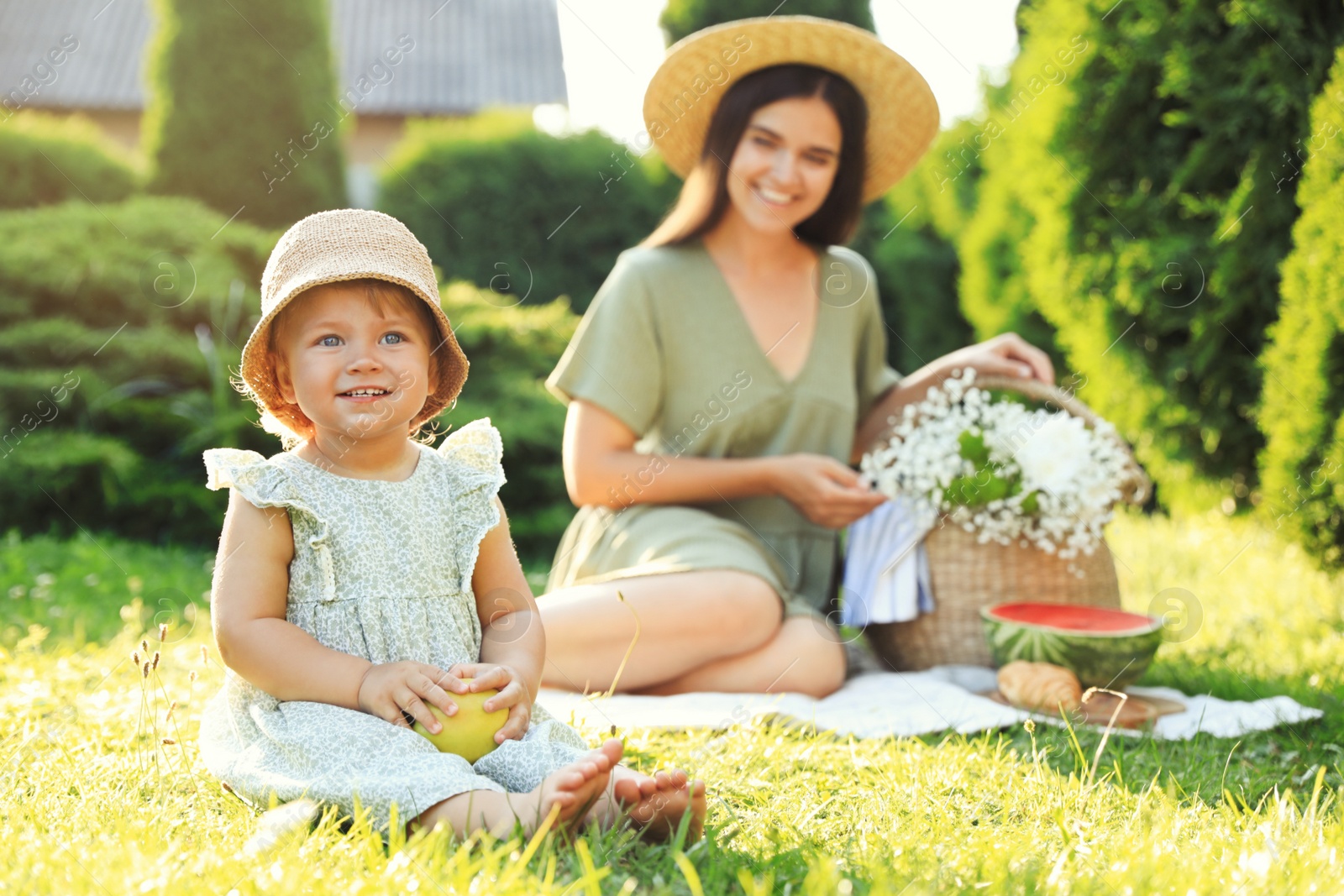 Photo of Mother and her daughter having picnic in garden, focus on baby with apple