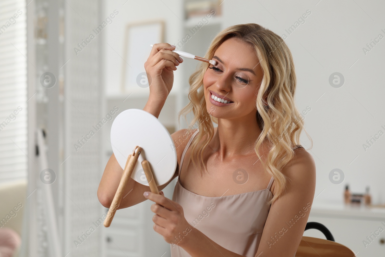 Photo of Beautiful makeup. Smiling woman applying eyeshadows in front of mirror indoors