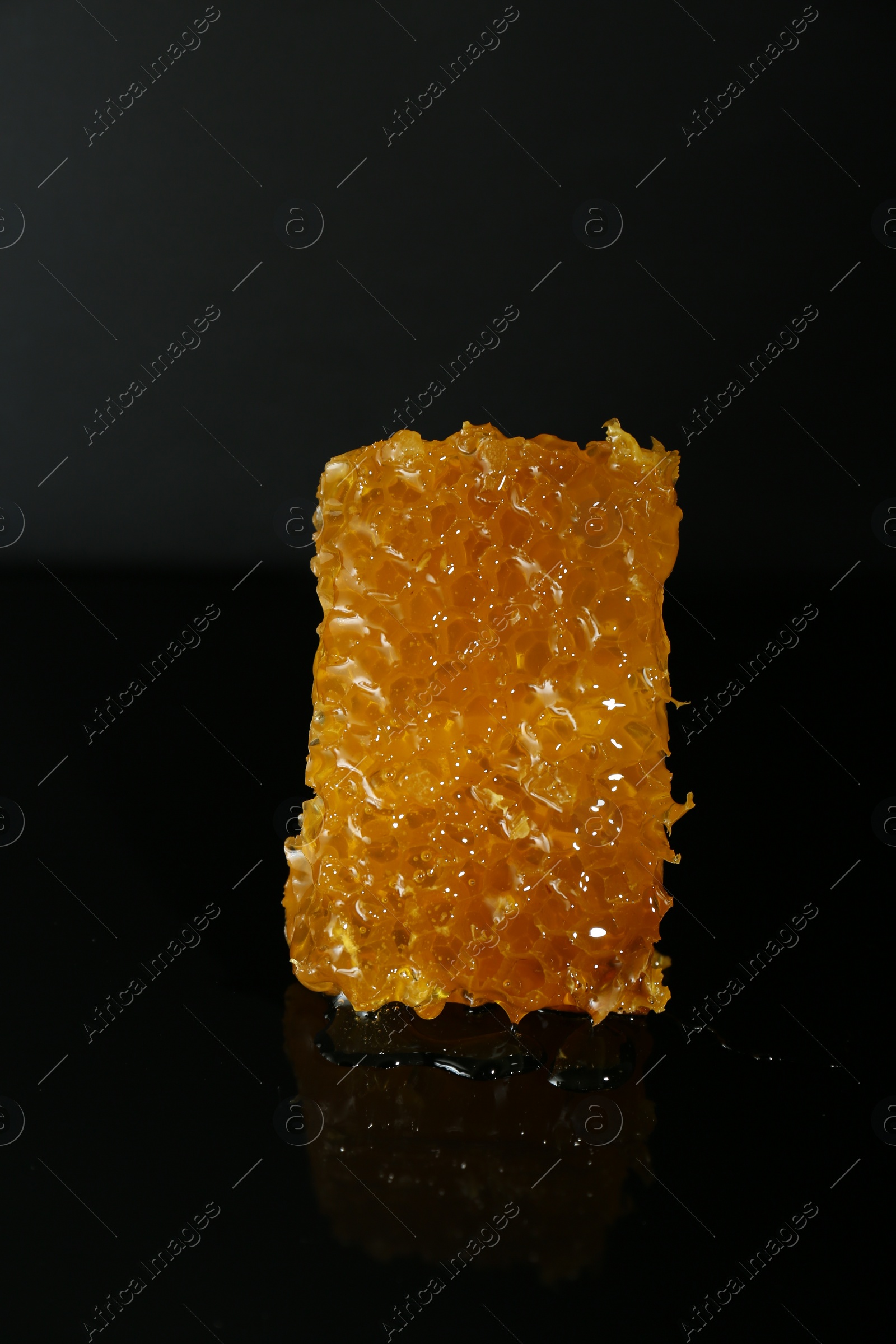 Photo of Piece of natural honeycomb with tasty honey on black background