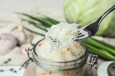 Photo of Fork with tasty fermented cabbage over jar, closeup