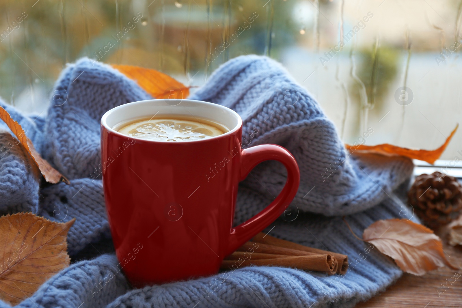 Photo of Cup of hot drink, sweater and autumn leaves on windowsill. Cozy atmosphere