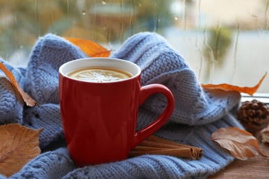 Photo of Cup of hot drink, sweater and autumn leaves on windowsill. Cozy atmosphere