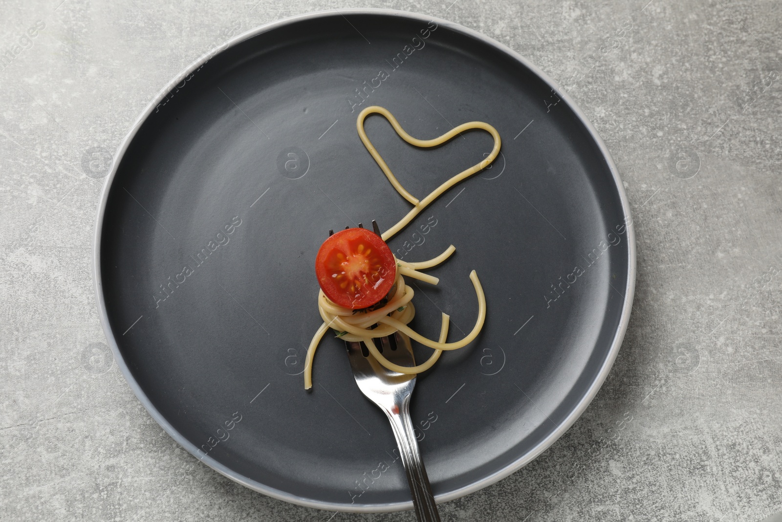 Photo of Heart made of tasty spaghetti, fork and tomato on light grey table, top view