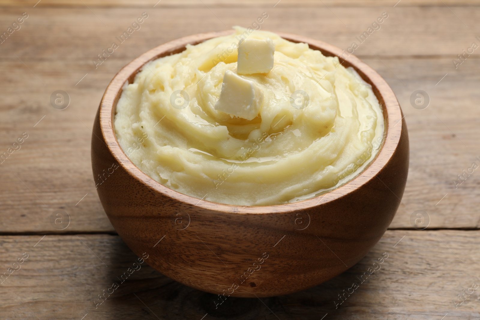 Photo of Bowl of delicious mashed potato with butter on wooden table, closeup