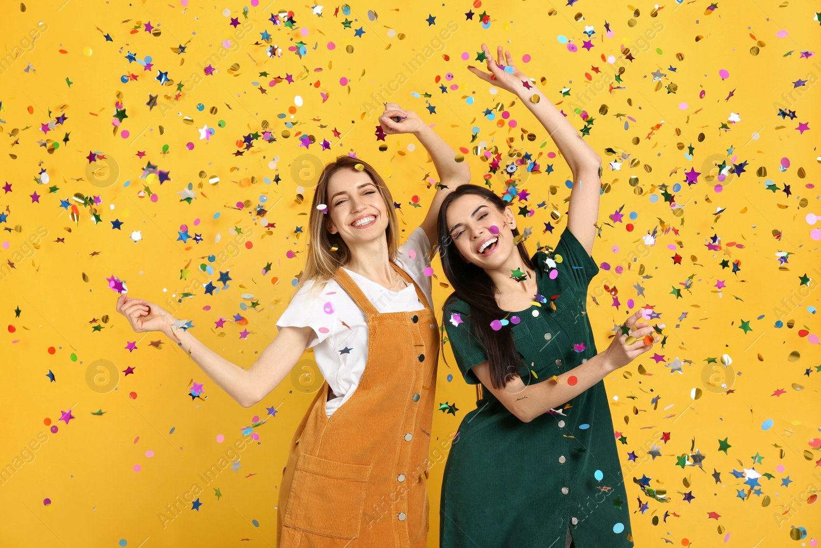 Photo of Happy women and falling confetti on yellow background