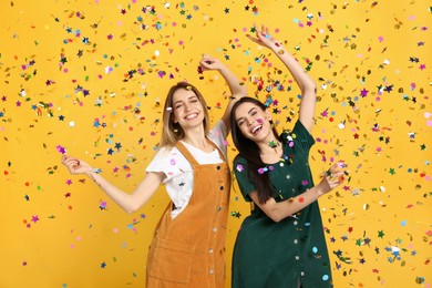 Photo of Happy women and falling confetti on yellow background